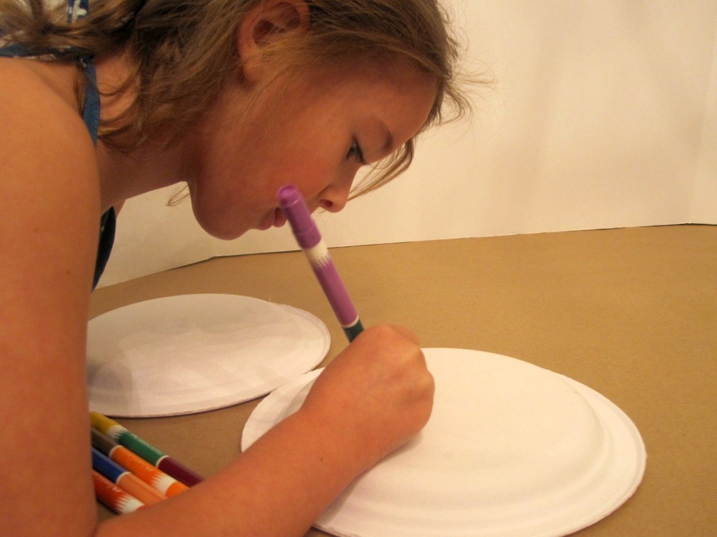 little girl making a paper plate tambourine